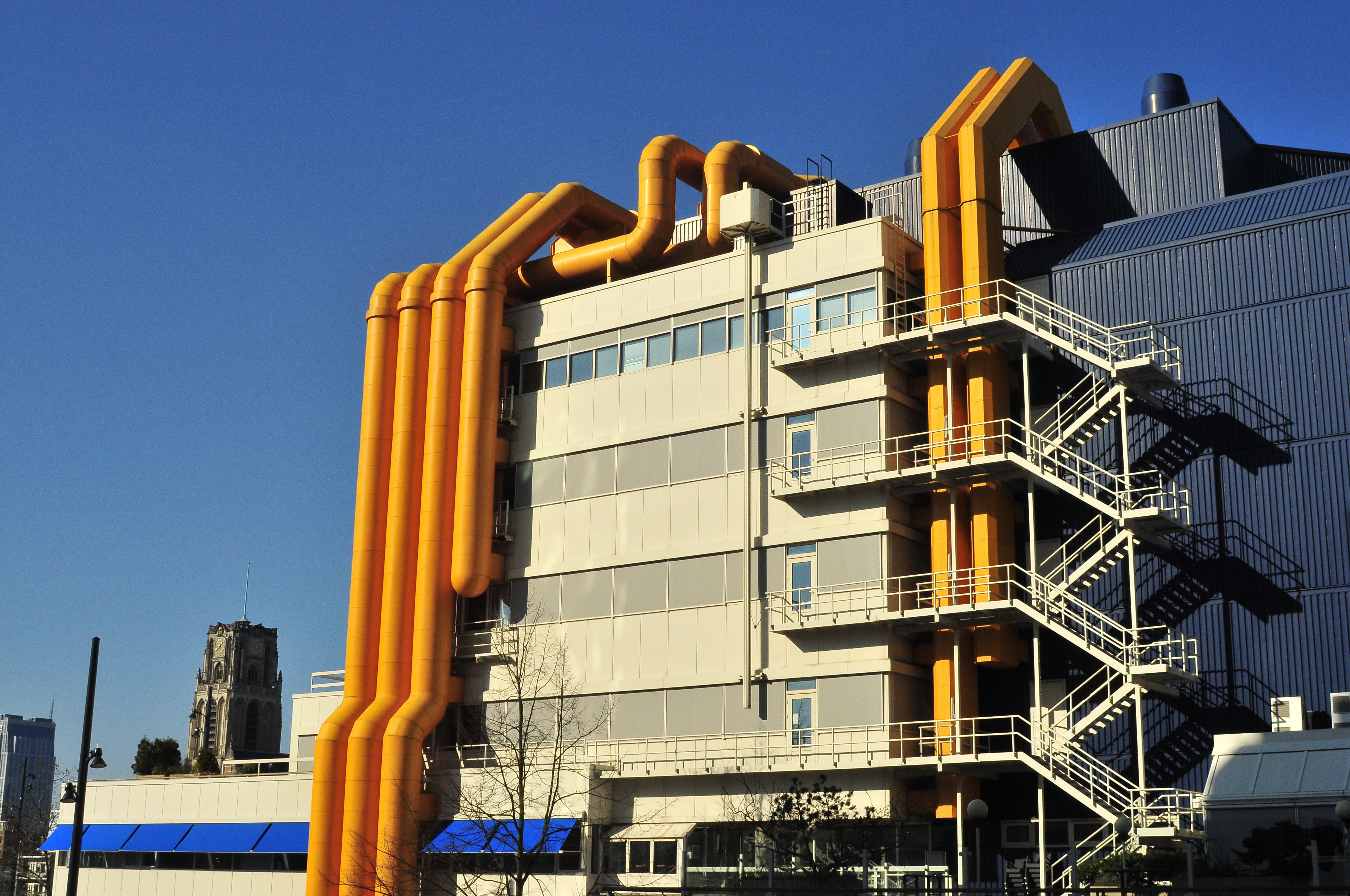 Photo of the Centrale Bibliotheek in Rotterdam, The Netherlands: an industrial looking building with metallic walls and various yellow pipes on the side.